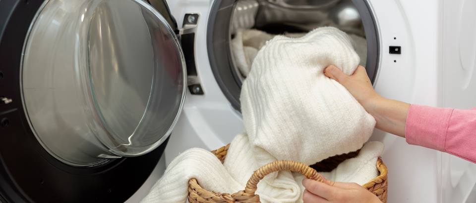 Frau legt weißen Pullover in eine Waschmaschine